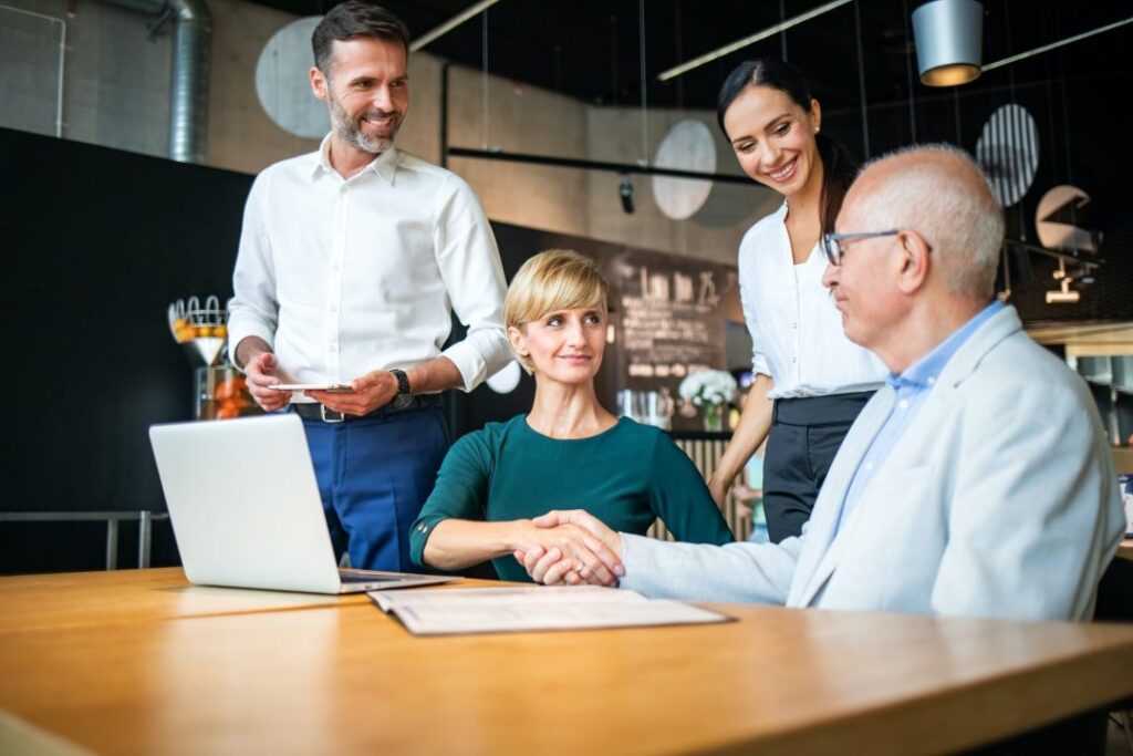 Person reviewing and signing loan documents beside laptop and smartphone.